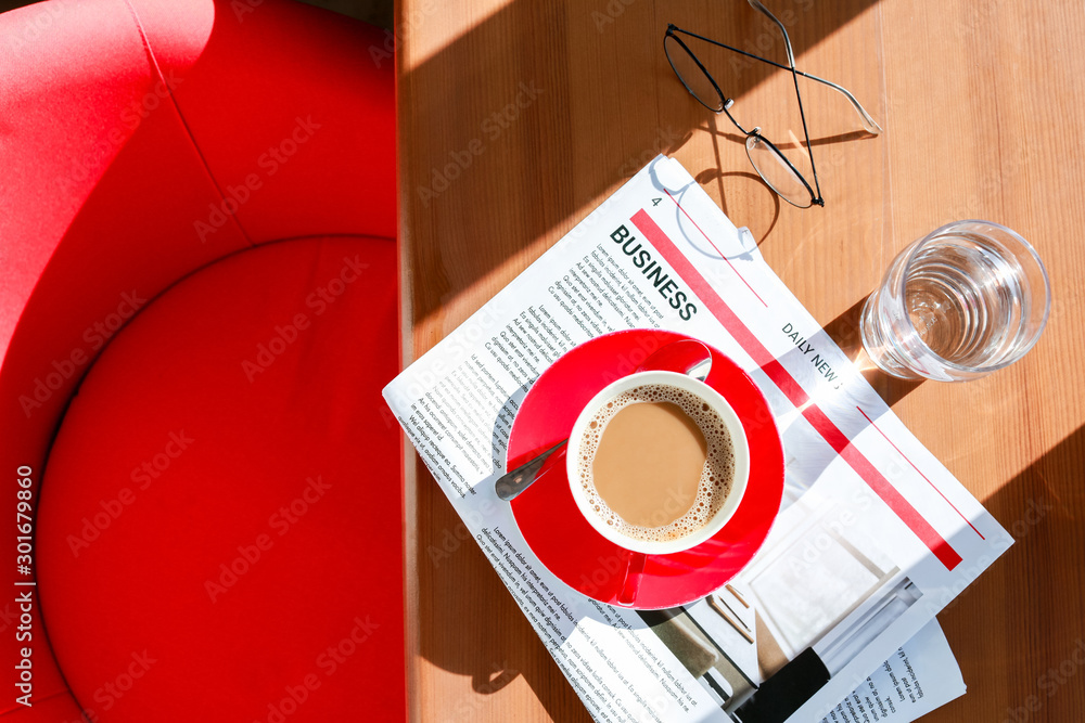 Cup of hot coffee, newspaper and glass of water on table in cafe