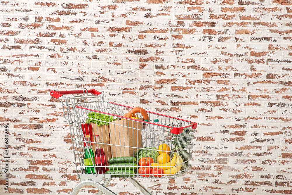 Shopping cart with products near brick wall