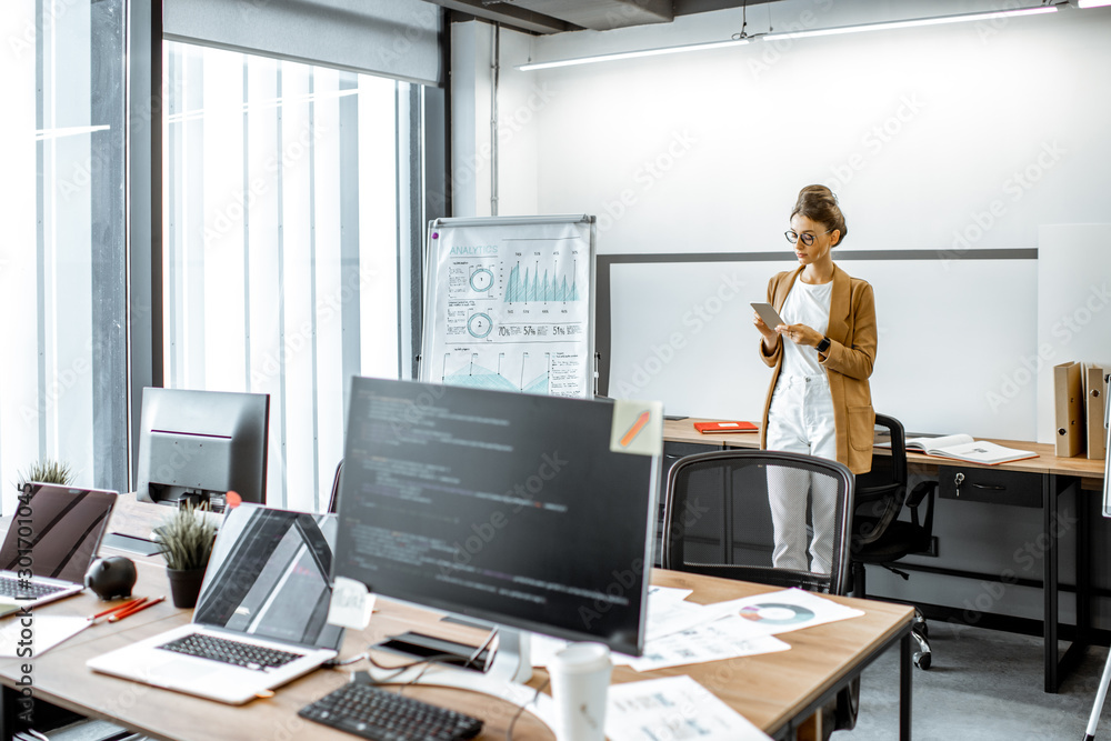 Young business woman preparing for a presentation, standing alone with phone near flipchart in the m