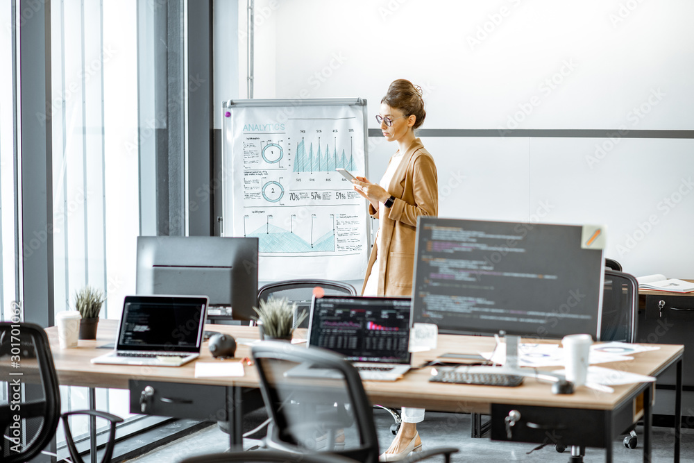 Young business woman preparing for a presentation, standing alone with phone near flipchart in the m