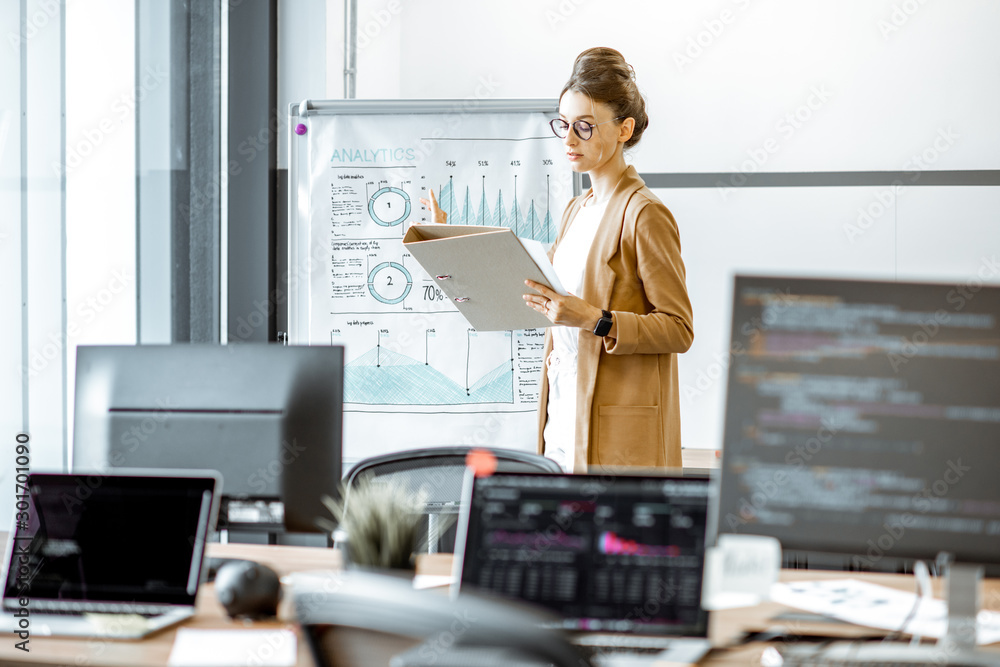 Young business woman preparing for a presentation, standing alone with documents near flipchart in t