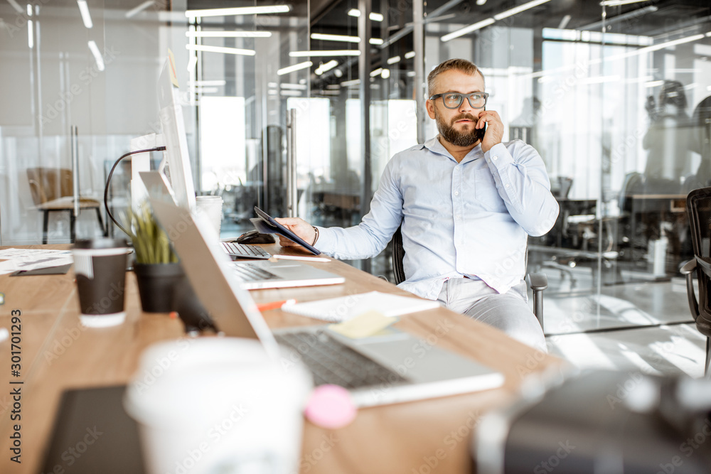 Senior confident manager talking on the phone while sitting at the working place in the modern offic