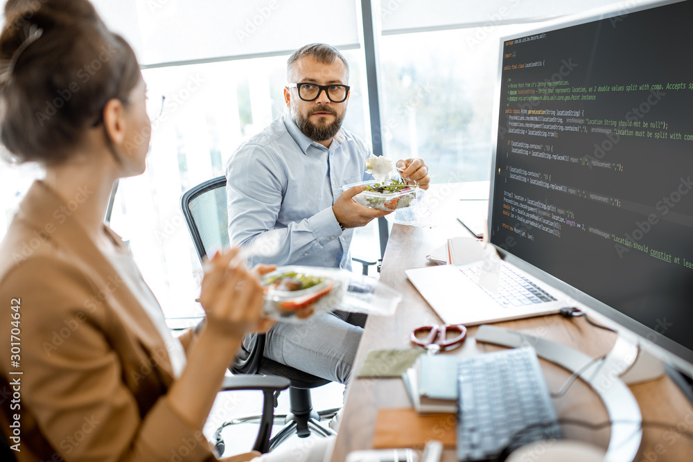 Man and woman eating salad during a lunch time on the working place without leaving the office