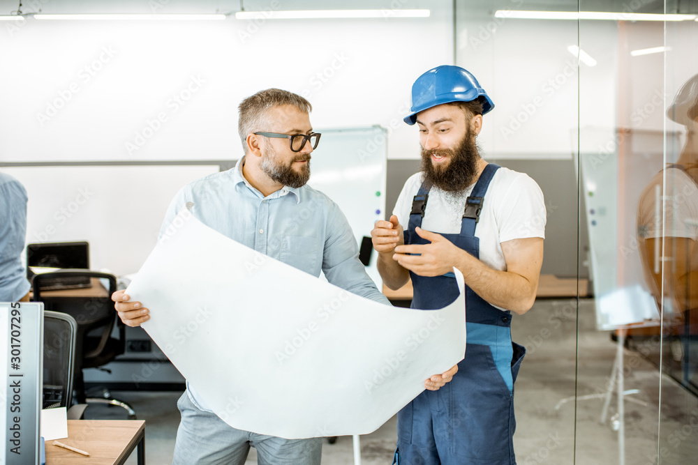 Senior foreman and workman in overalls working on project with blueprints in the office