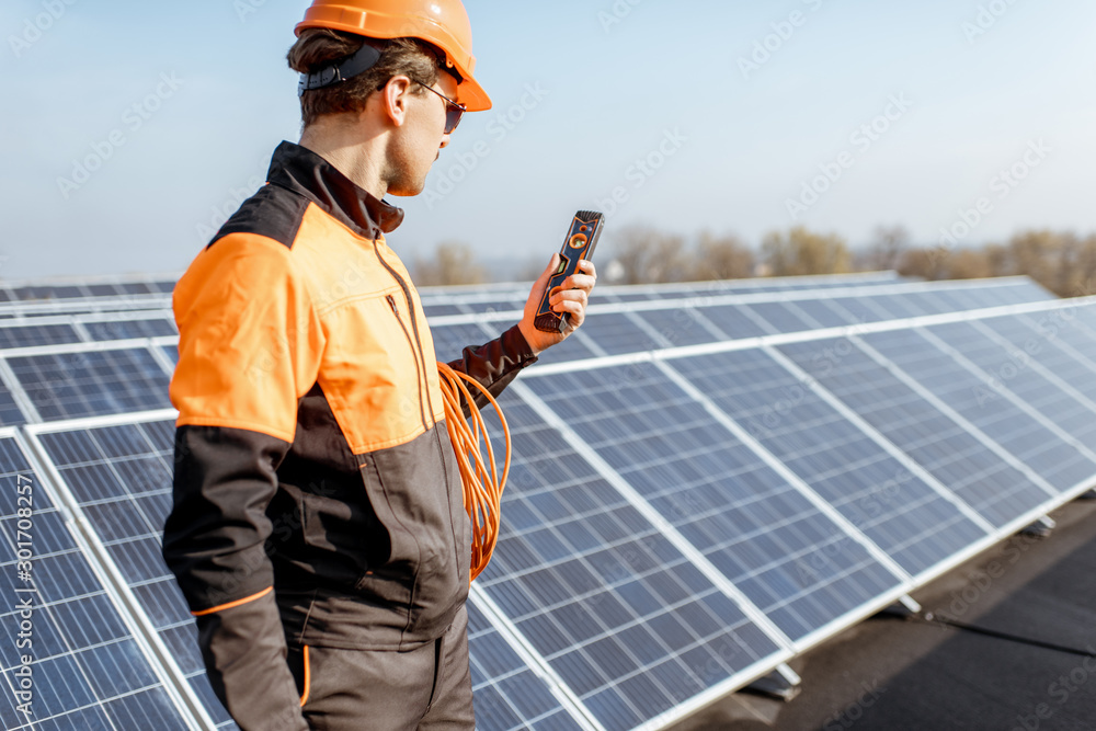 Well-equipped worker in protective orange clothing servicing solar panels on a photovoltaic rooftop 