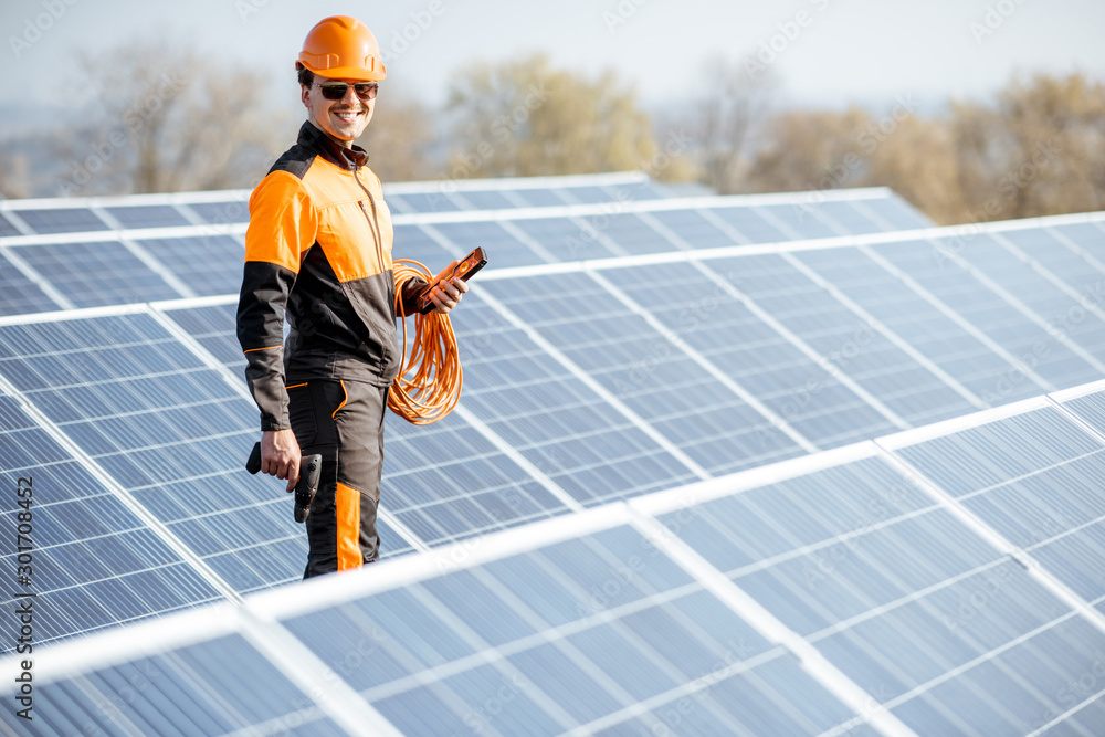 Portrait of a well-equipped worker in protective orange clothing examining solar panels on a photovo