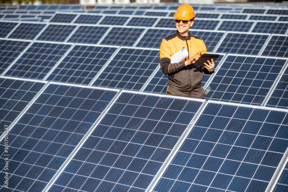 Engineer in protective workwear carrying out service of solar panels with digital tablet on a photov