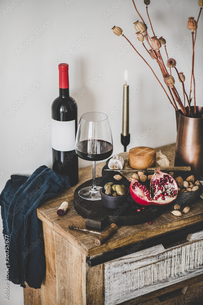 Wine and snack set. Glass and bottle of red wine, board with cheese, fruit, almonds and olives, deco