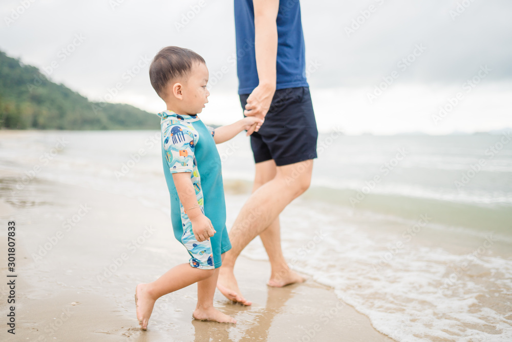 Asian toddler boy walking to the sea with his father.Dad holding hand his son for swim and play at t