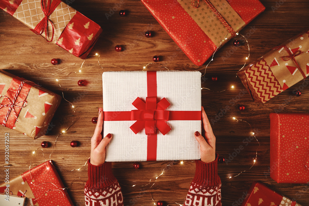 red Christmas gifts with hands and garlands of lights on wooden background.