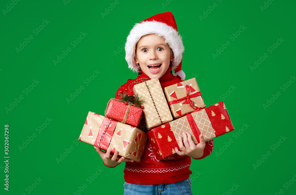 happy funny child girl in red Christmas hat   with gift on green   background.