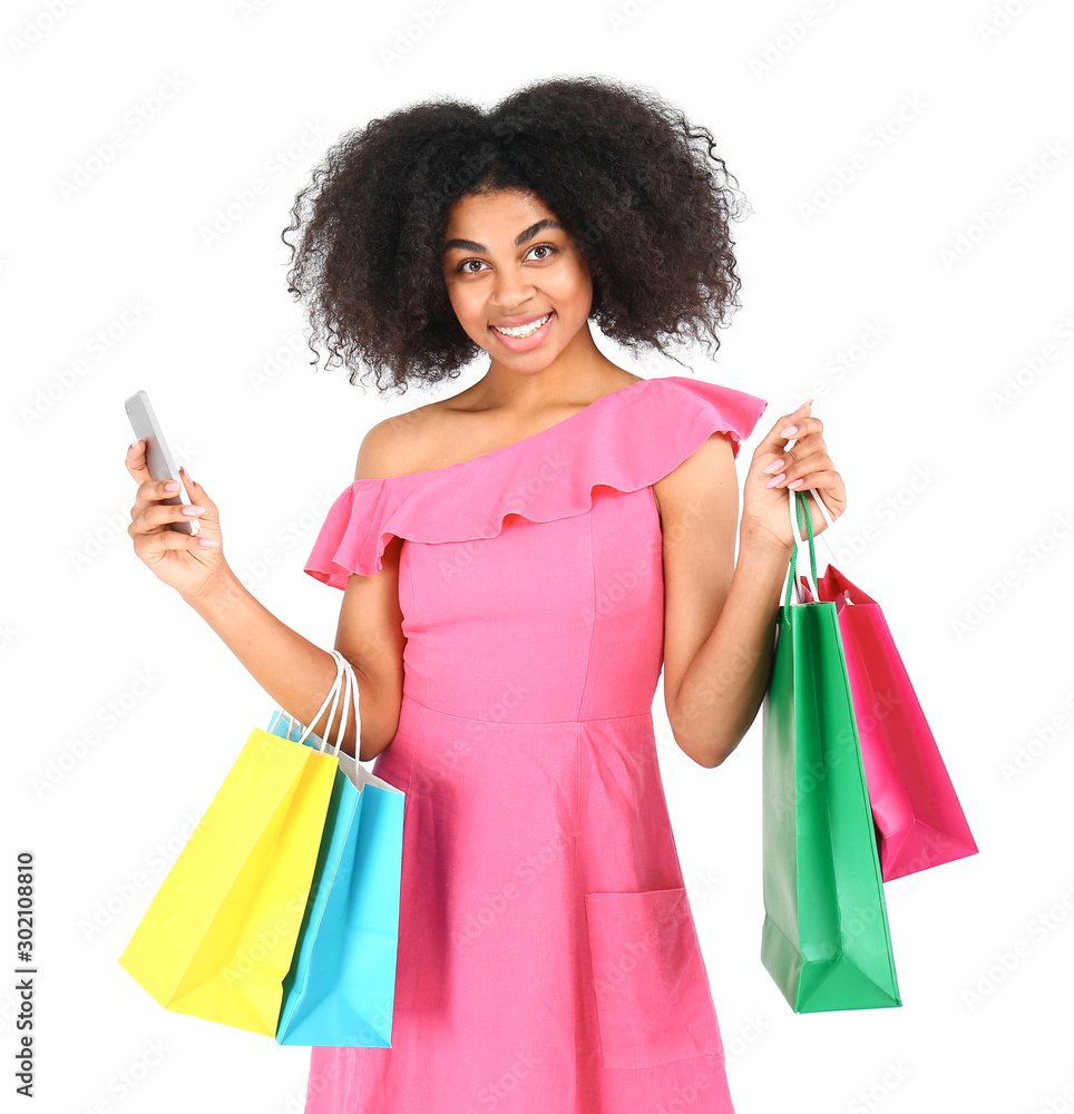 Beautiful African-American woman with shopping bags and mobile phone on white background