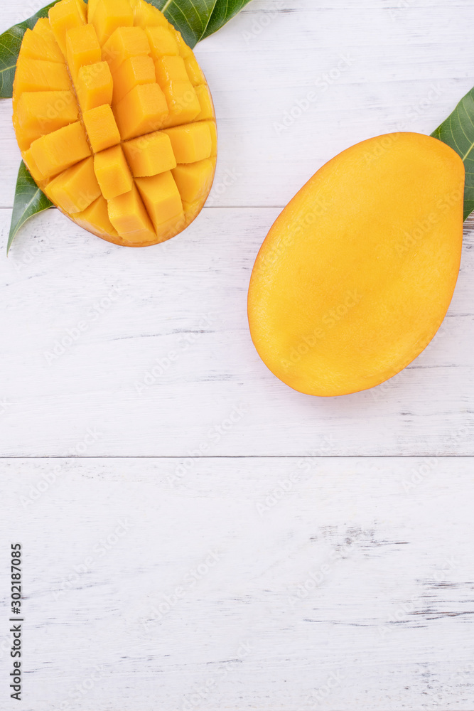 Beautiful chopped ripe mango with green leaves on bright white color wooden background, top view, fl