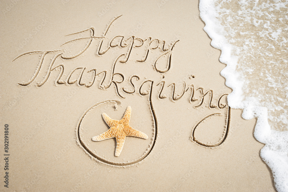 Happy Thanksgiving message handwritten on smooth sand beach with decorative starfish and oncoming wa