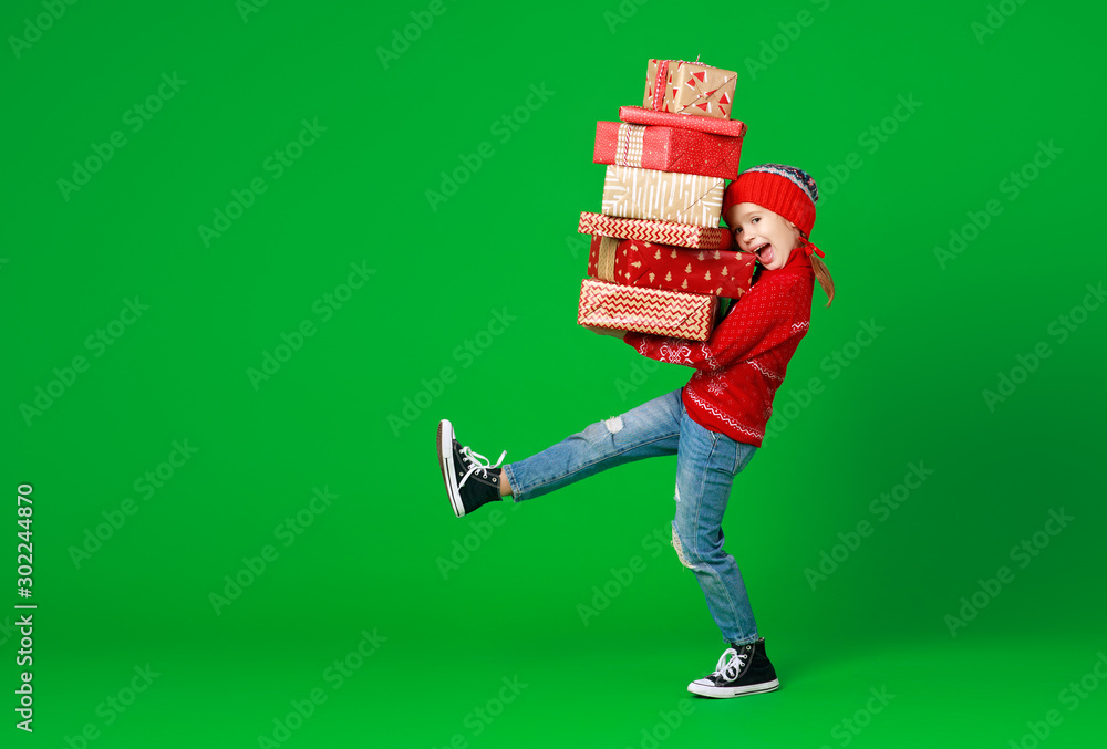 happy funny child girl in red Christmas hat   with gifts on green   background.