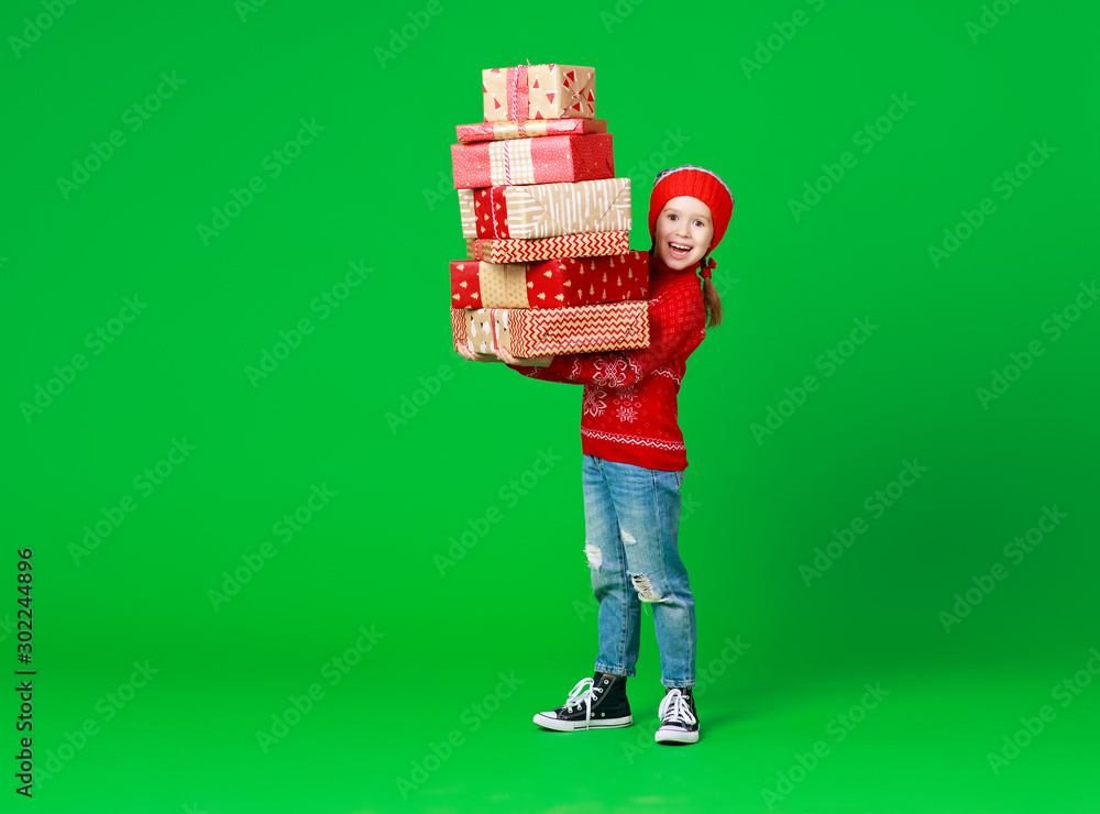 happy funny child girl in red Christmas hat   with gifts on green   background.