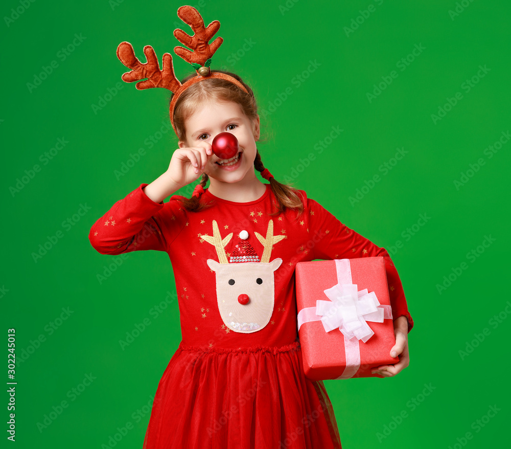 happy funny child girl in red Christmas reindeer costume with gift on green   background.