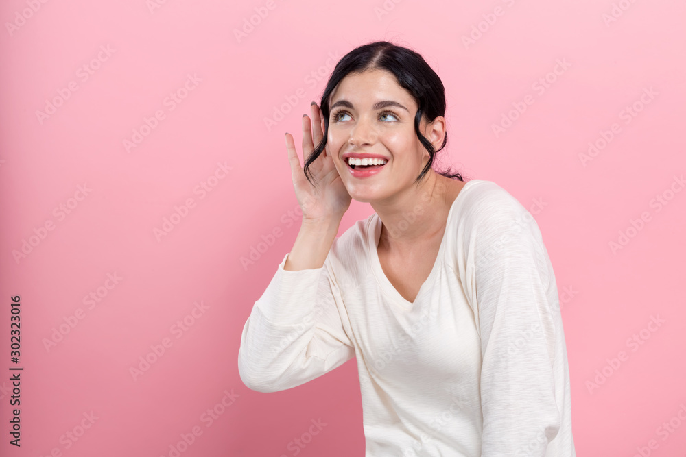 Young woman listening on a pink background