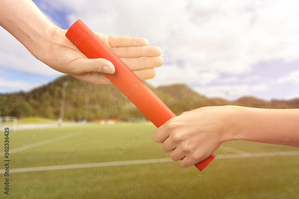 Relay baton being passed another person on a blurry background