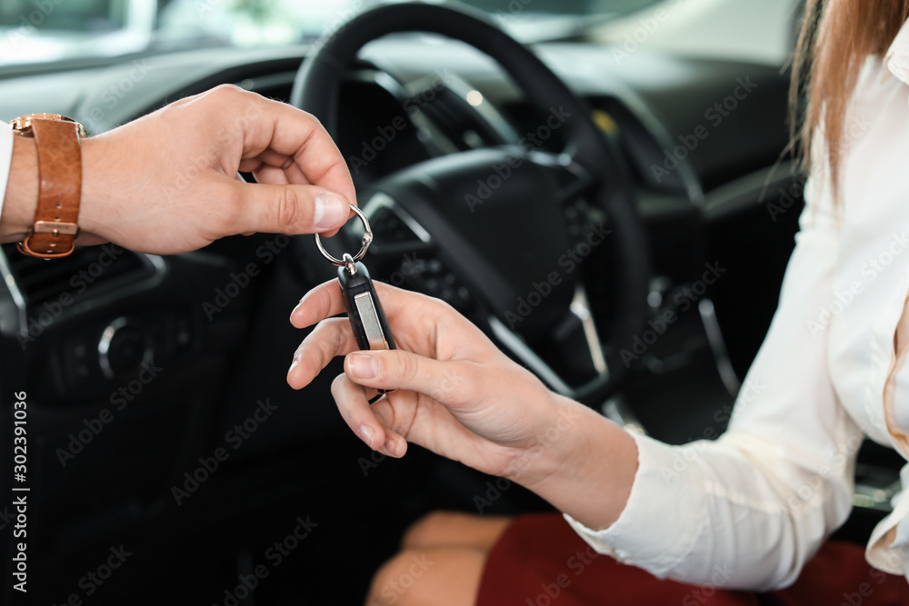 Salesman giving key from new car to young woman