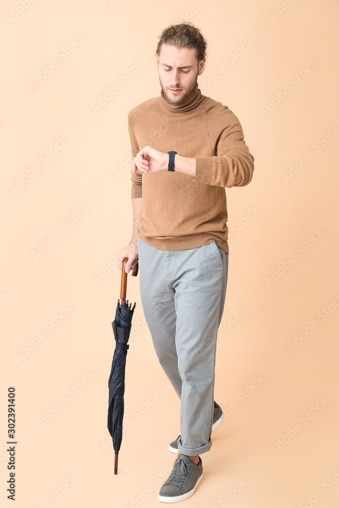 Portrait of handsome man with umbrella looking ob his watch on color background