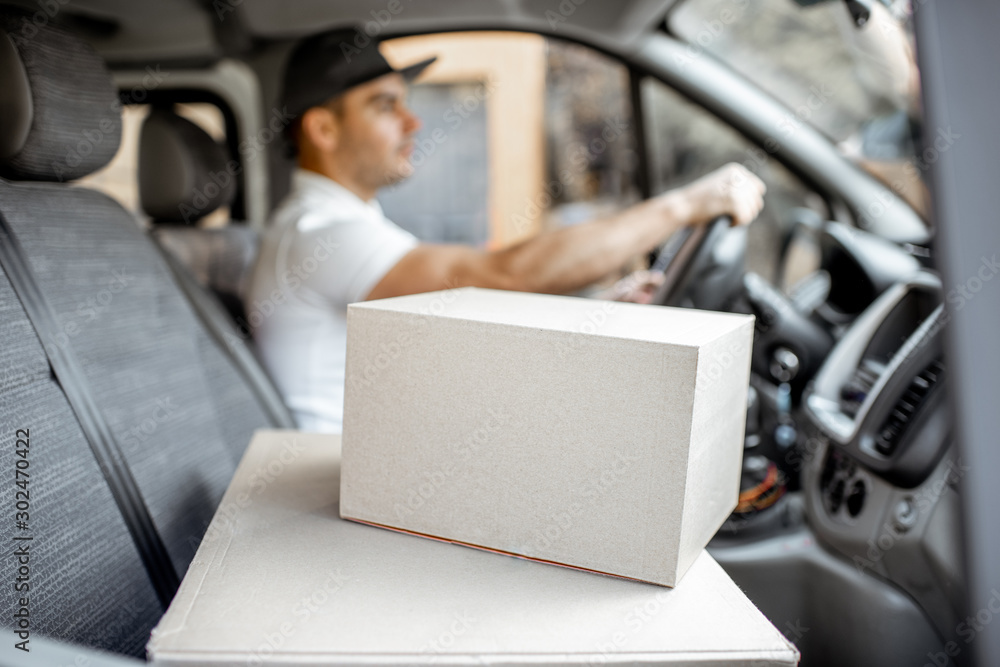 Delivery man driving cargo vehicle with parcels on the passenger seat, image focused on the cardboar