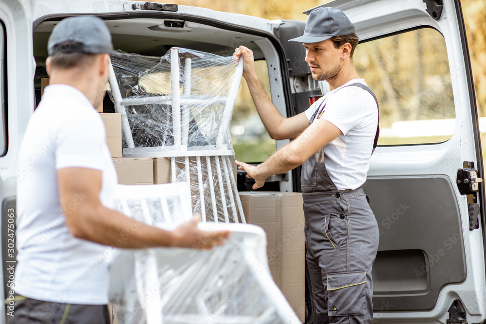 Delivery company employees unloading cargo van vehicle, delivering some goods and furniture to a cli