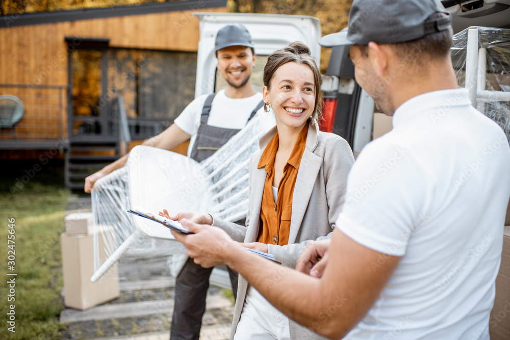 Delivery company employees unloading goods from a car trunk, delivering goods to a womans home. Hap