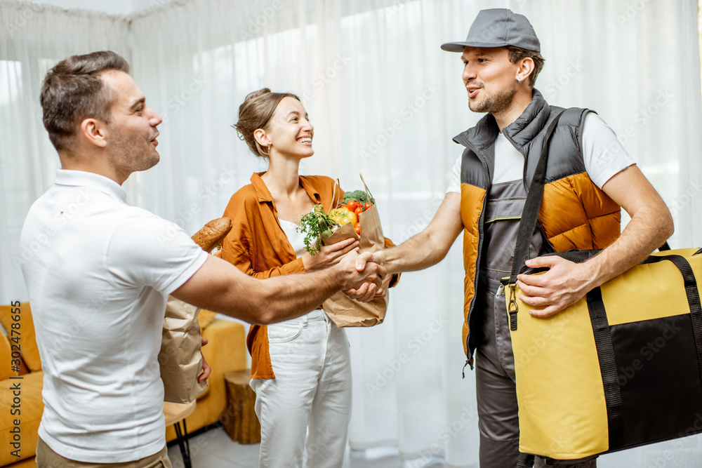 Cheerful courier in uniform delivering fresh groceries to a young family home. Online shopping and h