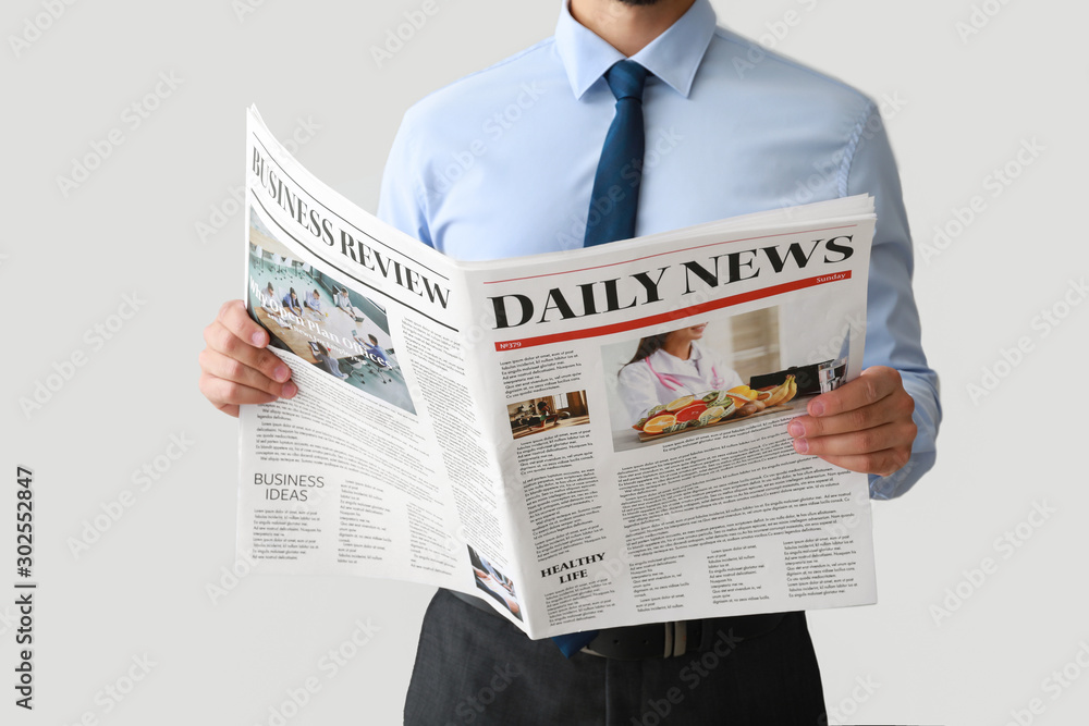 Handsome businessman with newspaper on light background