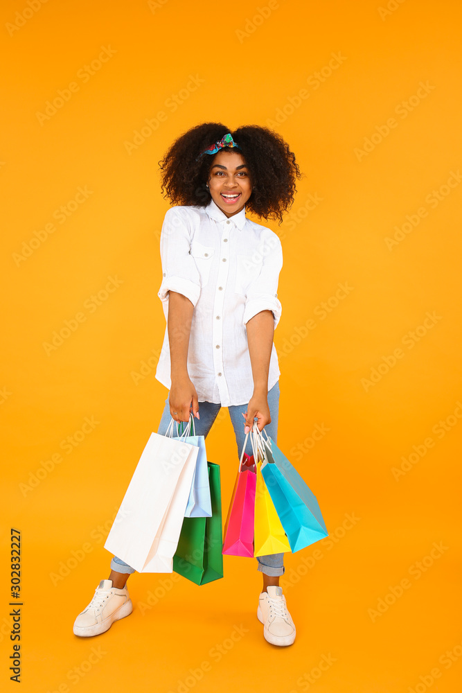 Beautiful African-American woman with shopping bags on color background