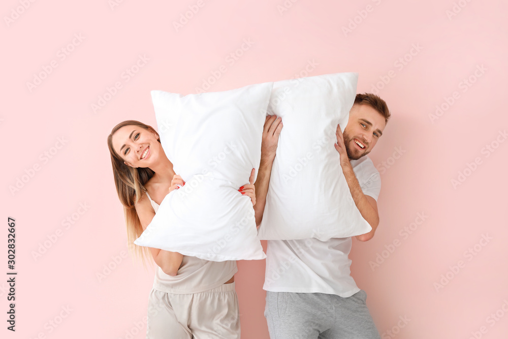 Young couple with pillows on color background