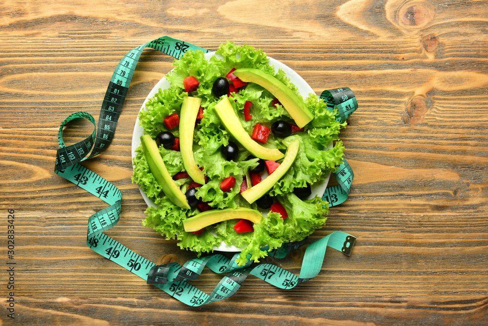 Plate with tasty avocado salad and measuring tape on wooden background