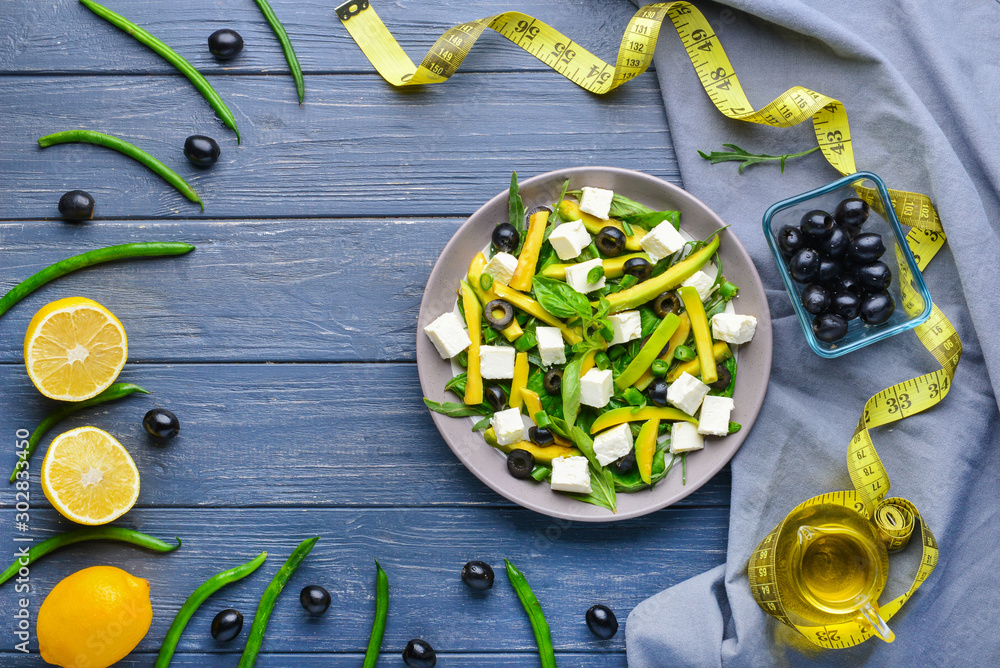 Plate with tasty avocado salad and measuring tape on wooden background