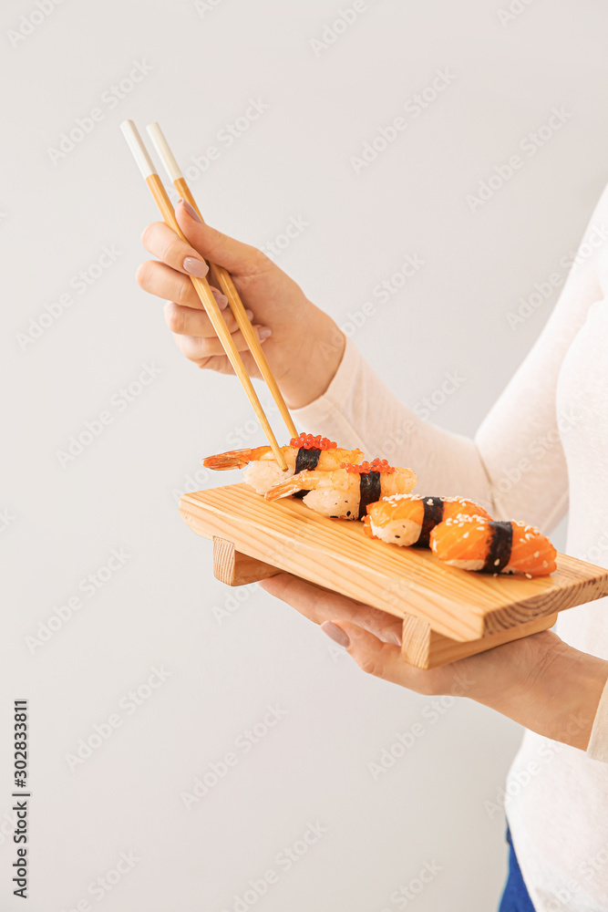 Woman with tasty sushi on light background