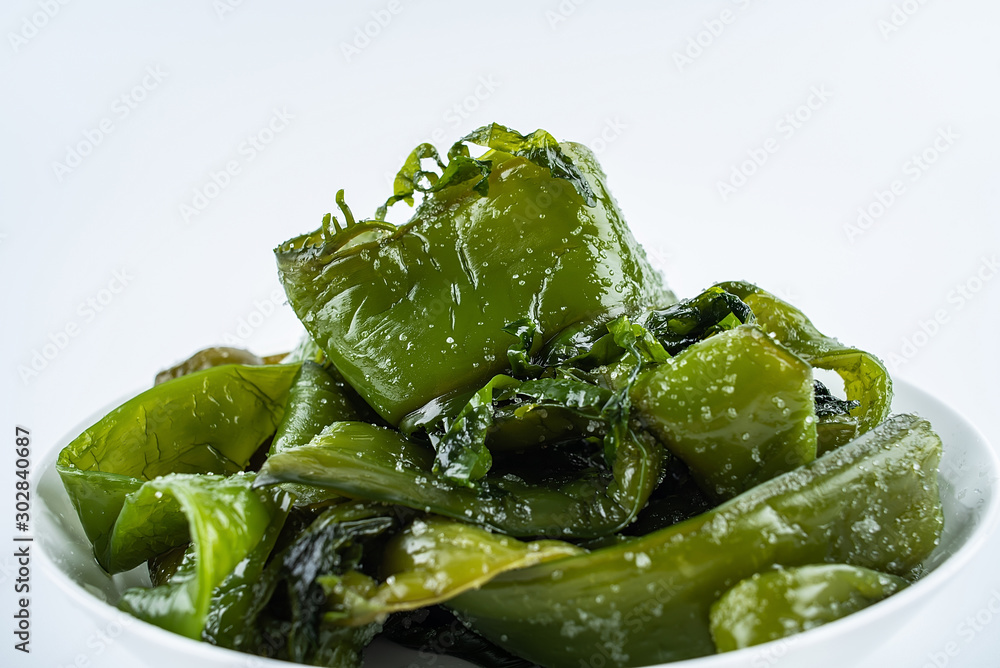 Fresh green salted sea cabbage stems on a saucer on a white background