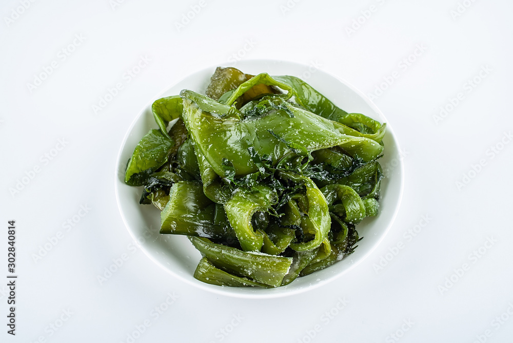 Fresh green salted sea cabbage stems on a saucer on a white background