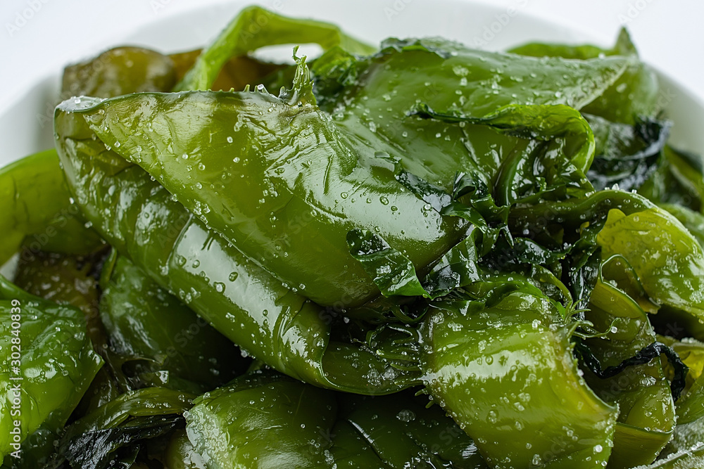 Fresh green salted sea cabbage stems on a saucer on a white background