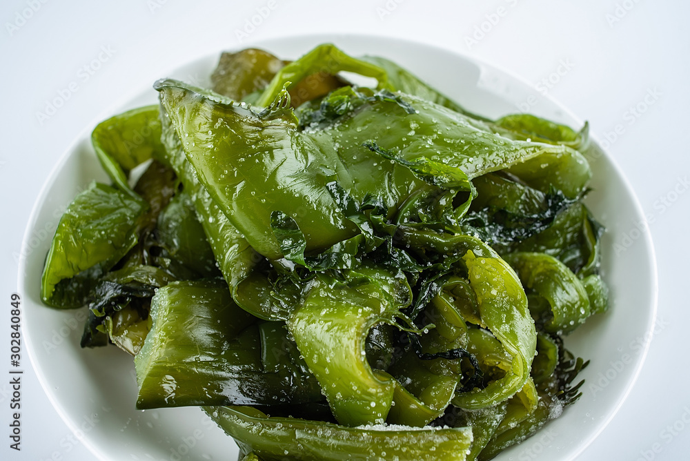 Fresh green salted sea cabbage stems on a saucer on a white background