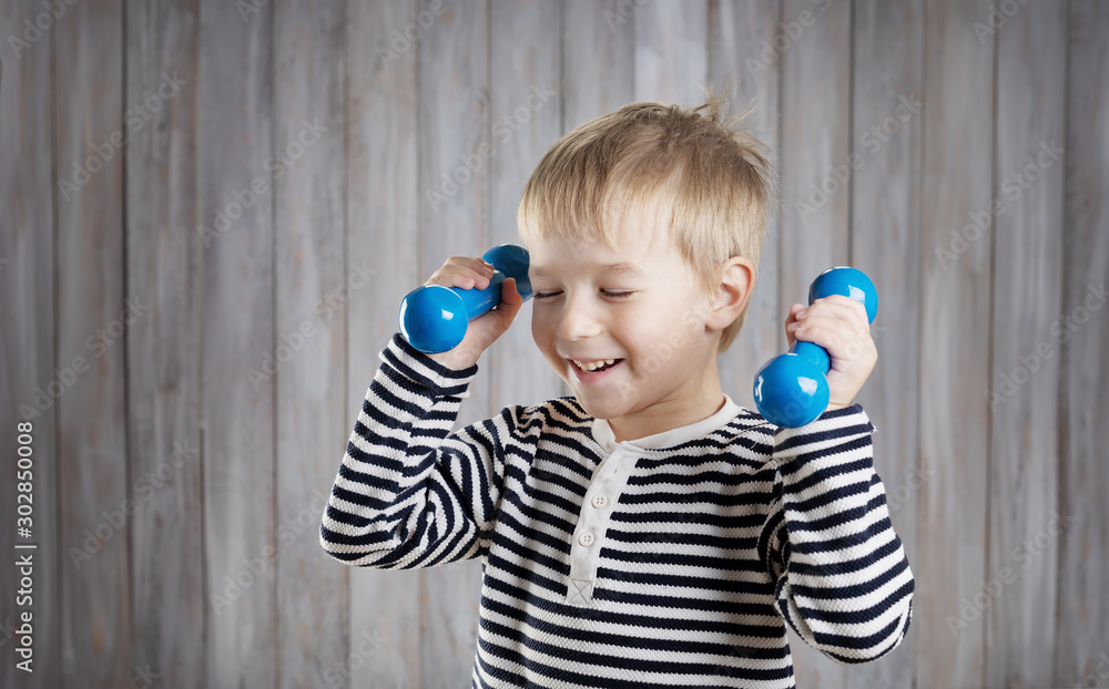 Child holding dumbbells indoors on wooden background.