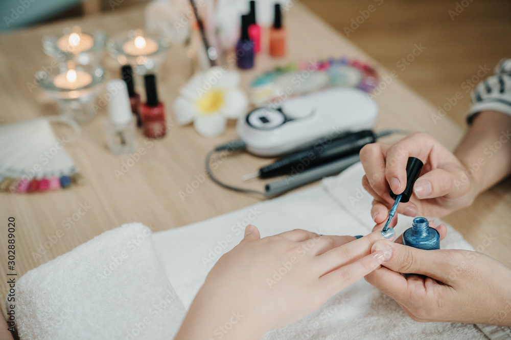 Closeup shot of woman beautician applying nail polish to female client on white towel in beauty spa 