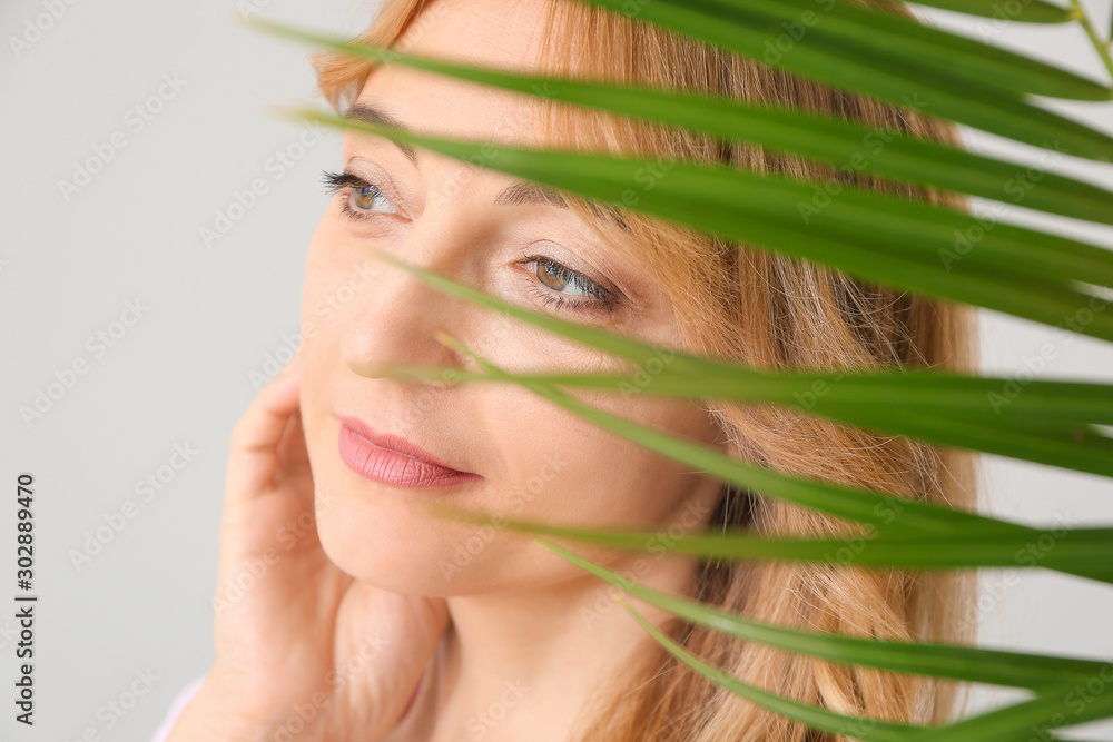 Mature woman with tropical leaf on light background