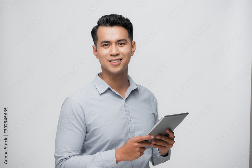 Photo of young happy man standing over white background using tablet computer.