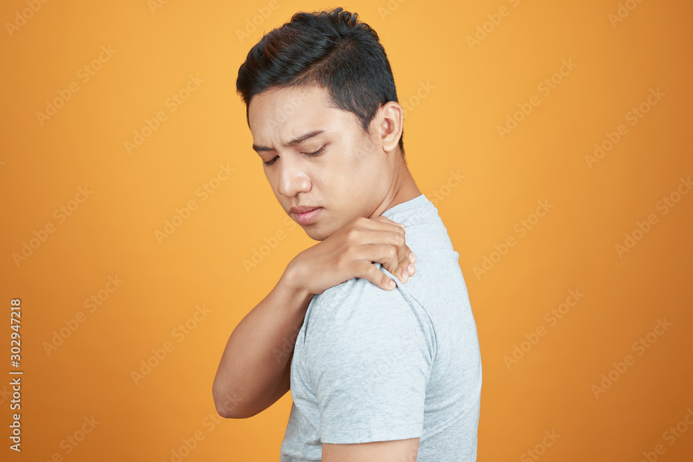 Young Asian man in casual with shoulder pain. Isolated on orange background