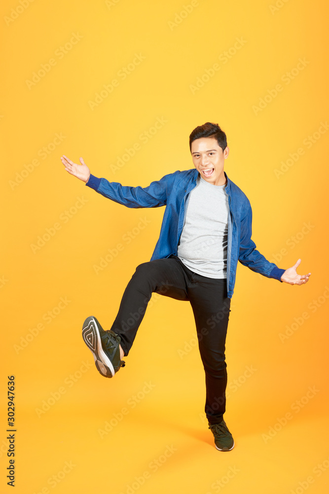 Full length portrait of an excited Asian man jumping over orange background