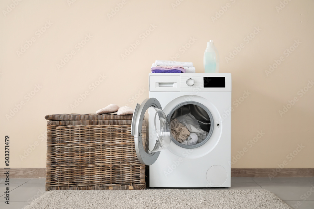 Modern washing machine with laundry near color wall