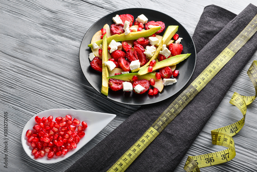 Plate with tasty avocado salad and measuring tape on wooden background