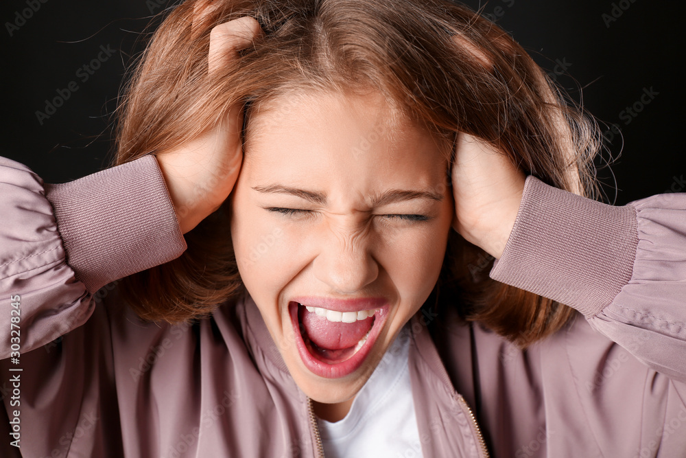 Screaming teenage girl on dark background, closeup