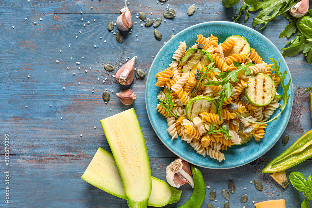 Plate with tasty pasta, vegetables and herbs on wooden table