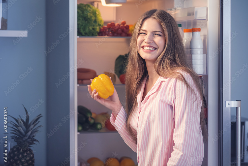 Beautiful young woman choosing food in refrigerator at night